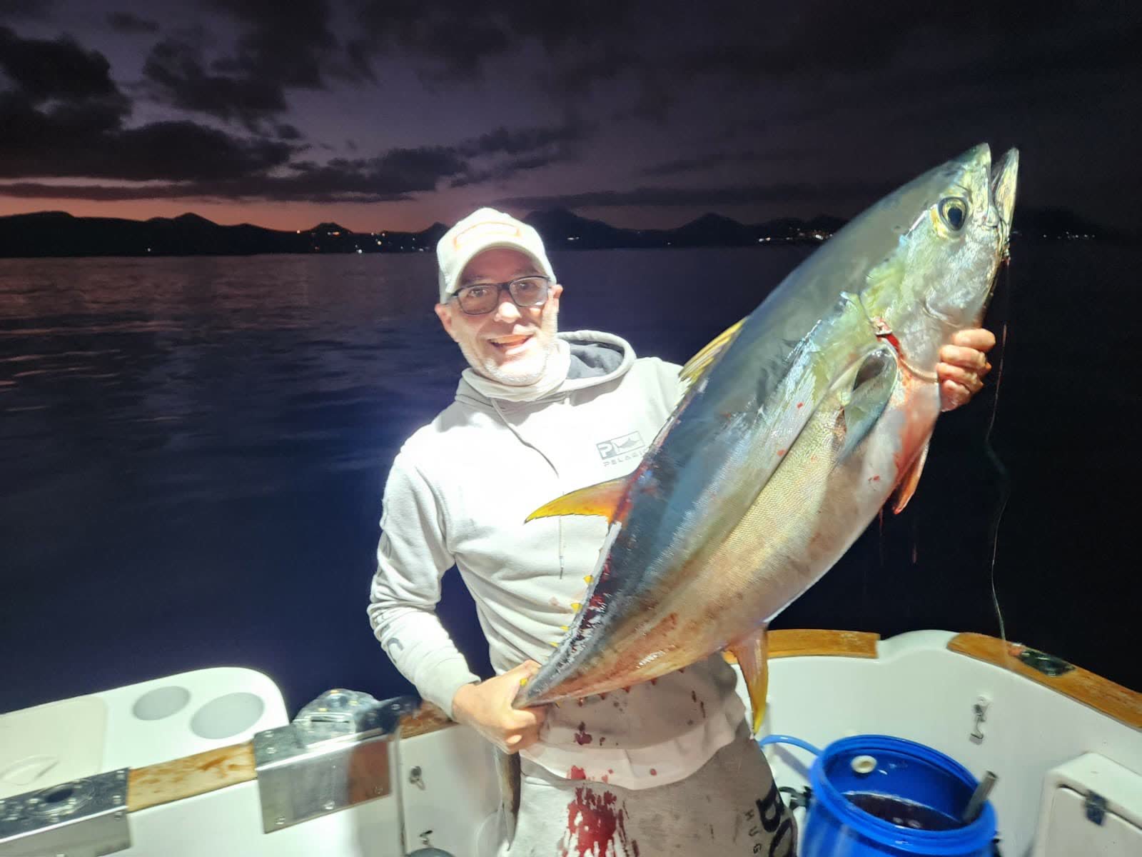 Angler holding a yellowfin tuna at dusk, long yellow sickle fins clearly visible